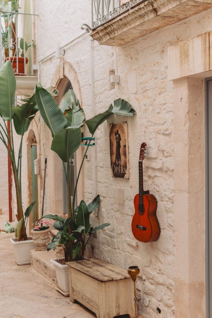Vicolo di un borgo pugliese imbiancato a calce con piante e una chitarra appesa al muro