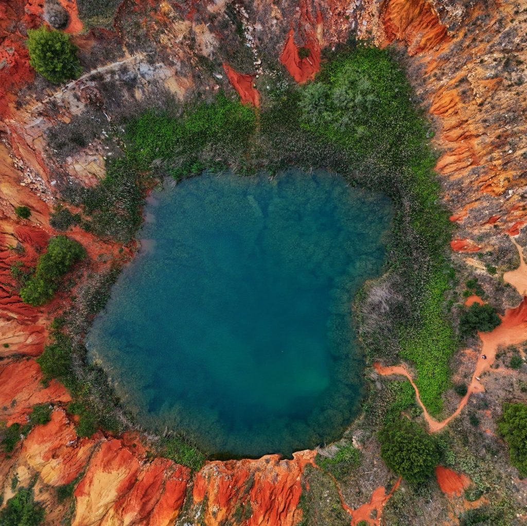 Il laghetto verde smeraldo della cava di bauxite di Otranto tra pareti rosse, dall'alto