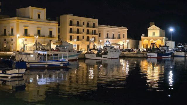Barche da pesca ormeggiate nel porto di Gallipoli di sera, con le luci del borgo riflesse nell'acqua