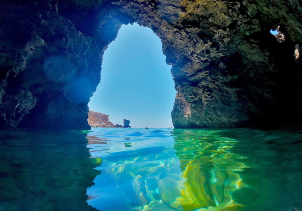 Grotta marina con acqua turchese e faraglione oltre l'arco di roccia