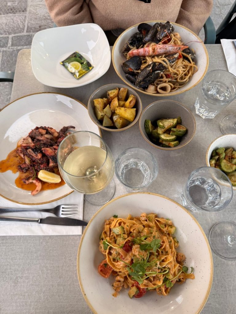 Tavola imbandita con linguine allo scoglio, polpo alla griglia, verdure e vino bianco